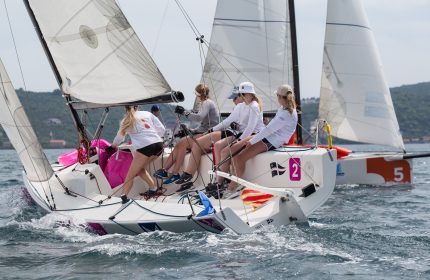 A high-speed moment: A girls' sailing team competes in a thrilling J70 boat race, neck and neck with another sailing boat.