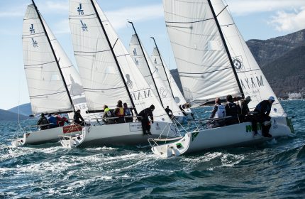 Close-up of J70 boats racing in a regatta, tightly grouped together on the water.